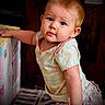 Phoenix is registered to the contest to win money with this photo: baby, child, infant, blue_eyes, curious, pastel_clothing, indoor, box, leaning, soft_expression, short_hair, person, cute, young_child, patterned_clothing, floor, wooden_background, portrait, standing, toddler