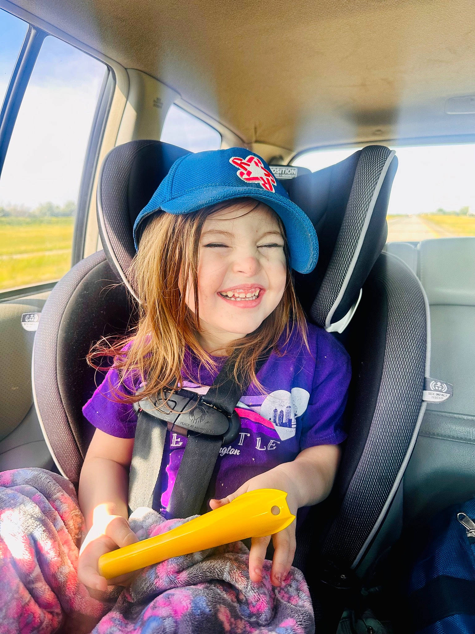 Audreyaunna is registered to the contest to win money with this photo: air_travel, auto_part, automotive_design, automotive_exterior, car, car_seat, car_seat_cover, electric_blue, fun, head_restraint, headwear, joy, leisure, motor_vehicle, person, purple, smile, steering_part, steering_wheel, toddler