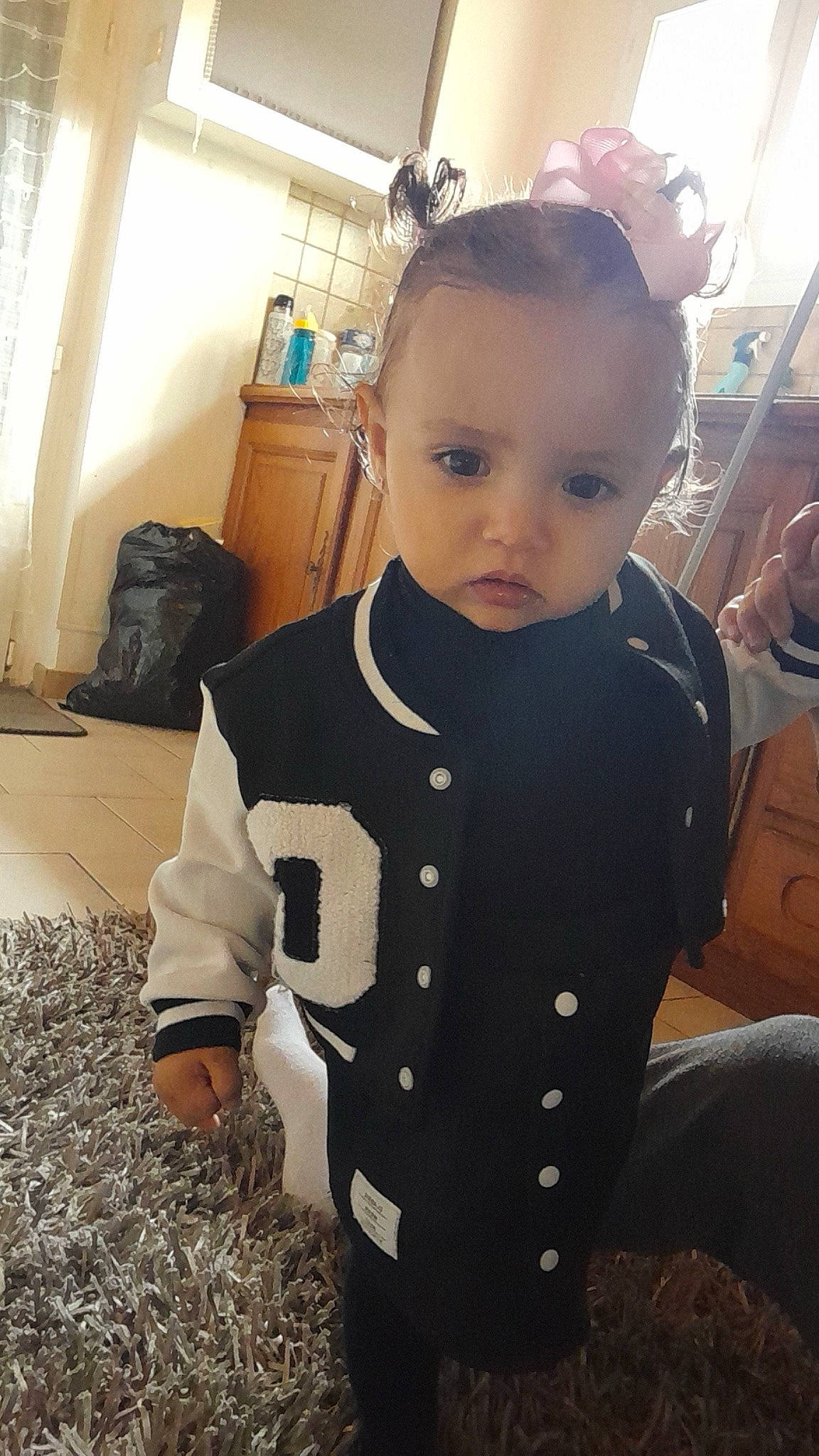 Yliana a rejoint le concours — aidez-le/la à gagner de superbes lots ! baby, baby_products, baby_toddler_clothing, cheek, child, facial_expression, flooring, happy, head, human_body, neck, pattern, person, personal_protective_equipment, room, sitting, skin, sleeve, standing, t_shirt