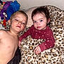 child, baby, blanket, leopard_print, plush_toys, shirtless, maroon_clothing, bedroom, cute, indoor, siblings, resting, portrait, face, blue_eyes, hair, hand, wall, soft_texture, comfort