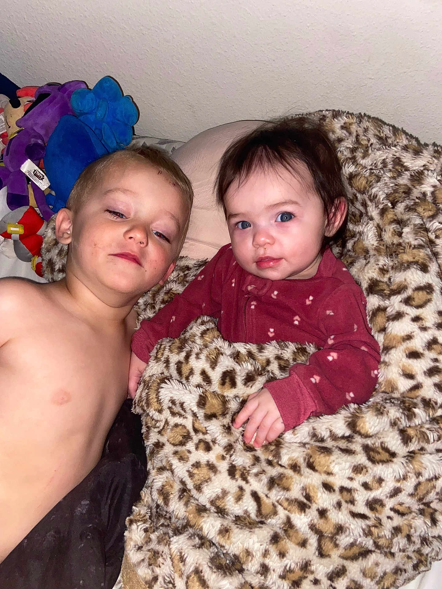 Aleah is registered to the contest to win money with this photo: child, baby, blanket, leopard_print, plush_toys, shirtless, maroon_clothing, bedroom, cute, indoor, siblings, resting, portrait, face, blue_eyes, hair, hand, wall, soft_texture, comfort