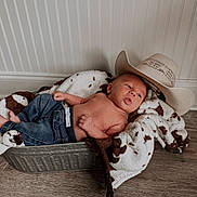 Stetson is registered to the contest to win money with this photo: baby, infant, jeans, blanket, cowboy_hat, metal_tub, wooden_floor, wall_paneling, tongue_out, shirtless, cozy, indoor, child, newborn, cute, relaxed, resting, portrait, small, hat