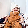 Stetson is registered to the contest to win money with this photo: baby, child, smiling, drool, overalls, knit_hat, blanket, indoors, happy, person, cute, face, sitting, cozy, warm_clothing, infant, white_wall, patterned_blanket, casual, portrait