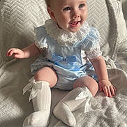 Riley is registered to the contest to win money with this photo: baby, blanket, blue_outfit, bows, child, clothing, cozy, cute, face, happy, head, indoor, infant, lace, person, portrait, sitting, smiling, soft_lighting, white_socks