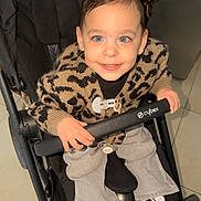 Alma participe au concours pour gagner de l'argent avec cette photo : child, toddler, stroller, smiling, blue_eyes, hair_buns, leopard_sweater, cardigan, jeans, sneakers, black_and_white_shoes, pacifier, hand, safety_bar, indoor, tile_floor, baby_carrier, cybex_brand, cute, portrait