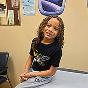 Maximus joined the competition — help win amazing prizes! child, smiling, curly_hair, medical_exam_table, clinic_room, space_wall_decal, tshirt, sweatpants, chair, wall_poster, indoor, young_person, happy, casual_clothing, healthcare, waiting_room, planet, star, window_decal, portrait