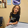 casual_clothing, chair, child, clinic_room, curly_hair, happy, healthcare, indoor, medical_exam_table, planet, portrait, smiling, space_wall_decal, star, sweatpants, tshirt, waiting_room, wall_poster, window_decal, young_person