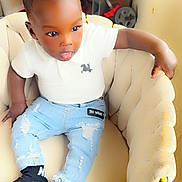 Zayden joined the competition — help win amazing prizes! toddler, child, sitting, white_polo, ripped_jeans, black_socks, chair, indoor, curly_hair, plush_chair, casual_clothing, young_child, home_interior, playful_expression, furniture, comfortable, relaxed, person, cute, small_child