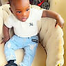 toddler, child, sitting, white_polo, ripped_jeans, black_socks, chair, indoor, curly_hair, plush_chair, casual_clothing, young_child, home_interior, playful_expression, furniture, comfortable, relaxed, person, cute, small_child
