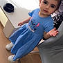 blue_dress, casual_clothing, chair, child, curious, cute, furniture, girl, hair_ties, indoor, person, pigtails, portrait, smiling, standing, table, toddler, white_shoes, wood_floor, young_child