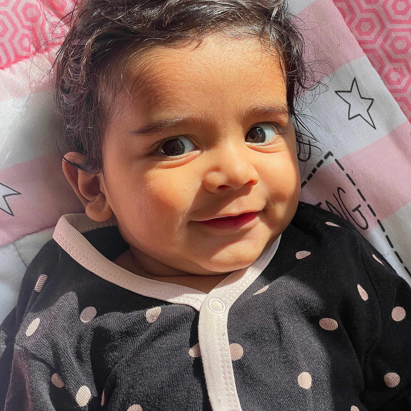 Ved is registered to the contest to win money with this photo: baby, black_clothing, blanket, child, cute, eyes, face, hair, happy, indoors, infant, pattern, person, pink_clothing, polka_dot, portrait, smile, star, sunlight, young