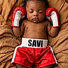 baby, infant, sleeping, boxing_gloves, boxing, red_shorts, sportswear, champion, portrait, lying_down, bed, blanket, brown_bedding, indoors, close_up, peaceful, cute, barefoot, text_on_clothing, photography