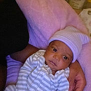 Zahari is registered to the contest to win money with this photo: baby, infant, striped_pajamas, hat, person, arm, pink_blanket, cozy, indoor, portrait, newborn, sleepwear, cute, soft_texture, child, resting, human, young, comfort, holding