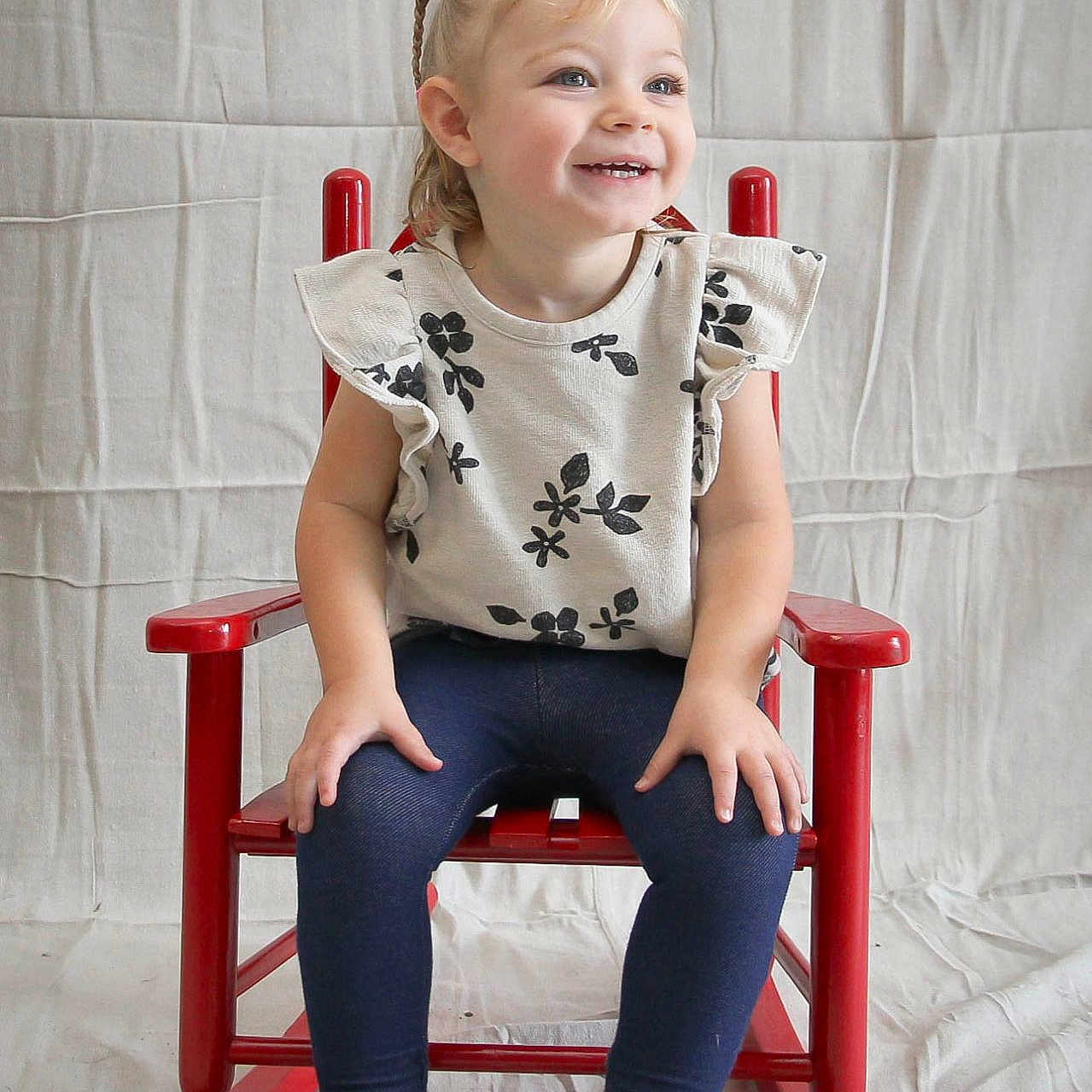 Lucie joined the competition — help win amazing prizes! child, toddler, girl, smiling, portrait, sitting, rocking_chair, red_chair, indoors, studio, white_background, floral_shirt, braided_hair, blonde_hair, blue_eyes, leggings, shoes, happy, looking_away, photography