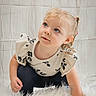 child, toddler, girl, portrait, sitting, smiling, blonde_hair, ponytail, blue_eyes, floral_clothing, dress, black_pants, indoor, studio, white_background, fluffy_rug, soft_lighting, photography, face, cute