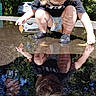 child, toddler, outdoor, puddle, reflection, water, leaves, nature, parked_car, trees, sunlight, crouching, exploring, black_clogs, shorts, t_shirt, blond_hair, face, splashing, photography