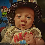 Jayson is registered to the contest to win money with this photo: baby, blue_wall, child, clip, closeup, clothing, container, curious, expression, face, hand, hat, indoor, infant, light, person, portrait, poster, sitting, toy