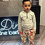 child, boy, hoodie, colorful_pants, sneakers, barbershop, neon_sign, floor, standing, indoor, haircut, casual_clothing, modern, young, curious_expression, fashion, portrait, lighting, concrete_wall, shop_interior