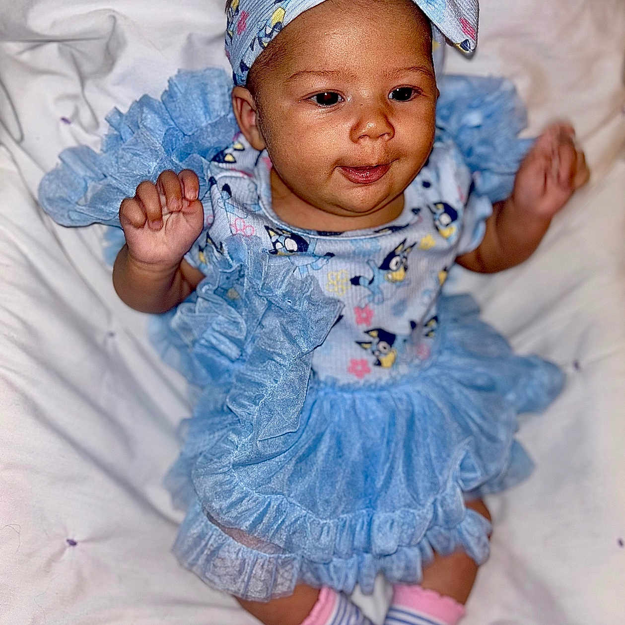 Isabella is registered to the contest to win money with this photo: baby, baby_girl, blue_dress, child, closeup, clothing, cute, frills, happy, headband, indoor, infant, person, pink, playful, portrait, smiling, socks, soft_blanket, striped_socks