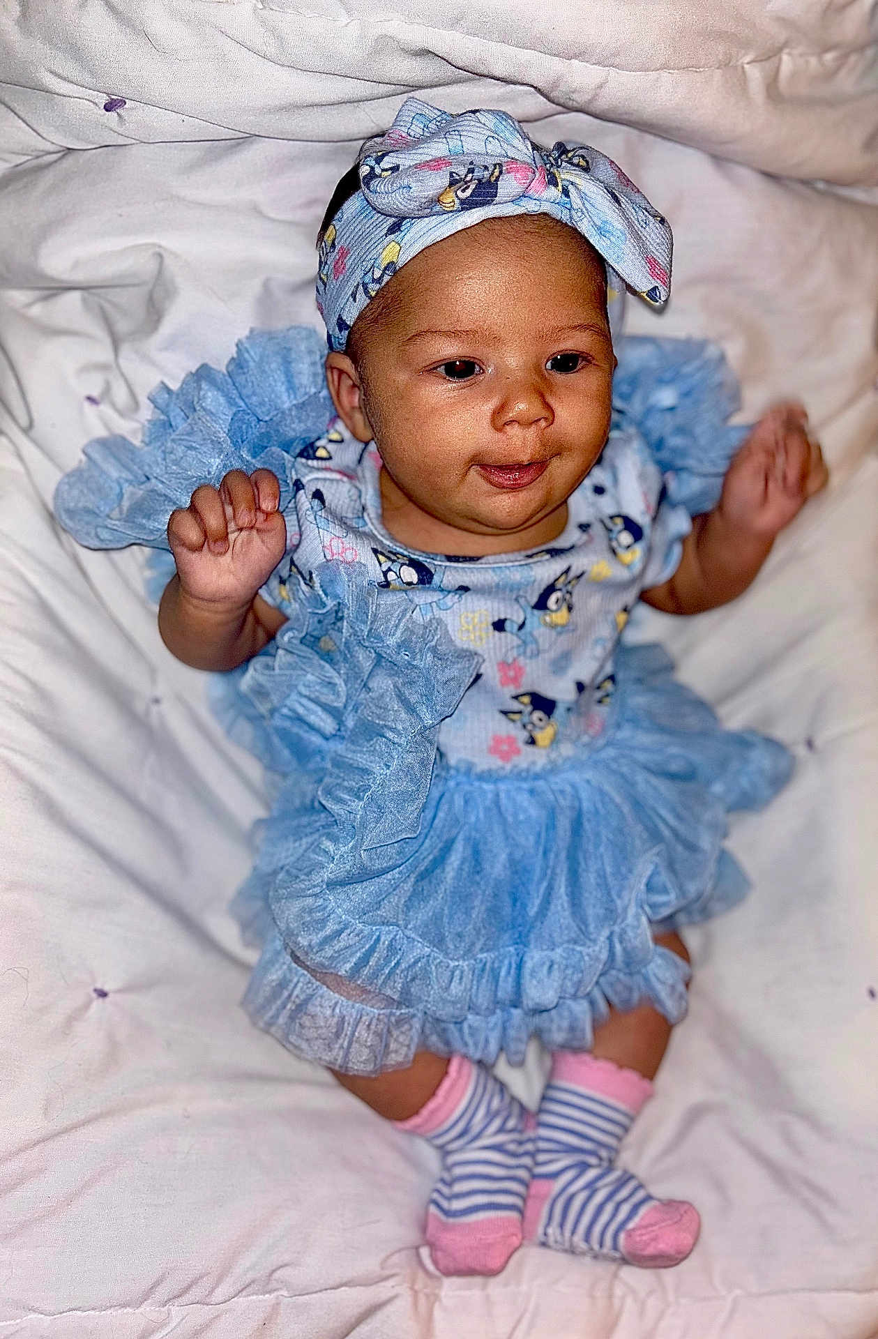 Isabella is registered to the contest to win money with this photo: baby, child, blue_dress, headband, socks, striped_socks, pink, frills, smiling, cute, infant, portrait, soft_blanket, indoor, happy, person, clothing, baby_girl, playful, closeup