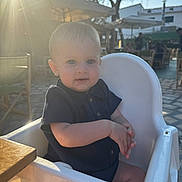 Tommy is registered to the contest to win money with this photo: baby, child, high_chair, outdoor, sunlight, sunflare, trees, umbrella, table, clothing, person, skin, face, seat, summer, daylight, restaurant, cute, infant, happy