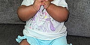 Jemma is registered to the contest to win money with this photo: baby, barefoot, blue_shorts, child, chubby_cheeks, clothing, couch, curly_hair, cute, gray_couch, hands_clasped, happy, indoor, infant, person, portrait, sitting, smiling, unicorn_shirt, young