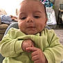 baby, child, infant, face, hands, green_jacket, indoor, living_room, couch, person, baby_swing, carpet, furniture, curious, cute, smile, chubby_cheeks, closeup, casual, relaxed