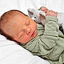 newborn, baby, sleeping, plush_toy, elephant, green_onesie, infant, peaceful, soft_texture, blanket, cute, child, portrait, resting, closeup, indoors, skin, hand, face, cozy