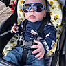 Junior is registered to the contest to win money with this photo: baby, sunglasses, stroller, infant, blue_jeans, blanket, bee_pattern, baby_clothes, face, tongue_out, child, casual, outdoor, seatbelt, cute, hands, cool, fashion, portrait, person