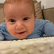 Elio joined the competition — help win amazing prizes! baby, infant, blue_onesie, blanket, face, eyes, smile, indoor, soft_texture, head, couch, curious, young_child, close_up, person, skin, child, happy, toddler, home