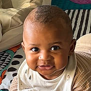 Issadya a rejoint le concours — aidez-le/la à gagner de superbes lots ! baby, infant, child, face, smile, eyes, clothing, bib, patterned_blanket, striped, cute, indoors, portrait, young, skin, hands, lying_down, head, expression, warm_light