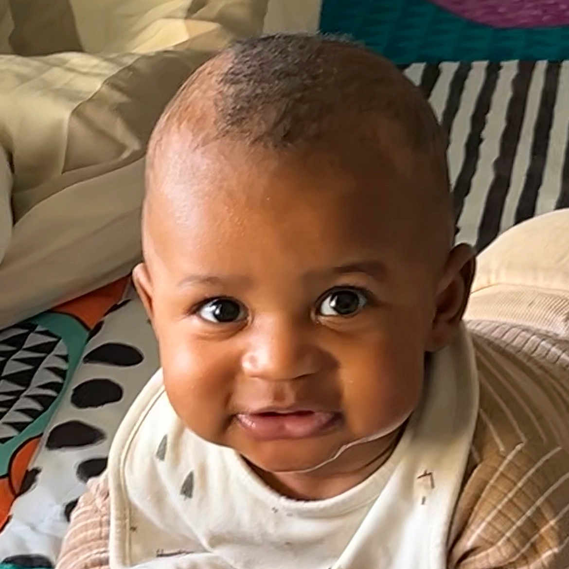 Issadya a rejoint le concours — aidez-le/la à gagner de superbes lots ! baby, bib, child, clothing, cute, expression, eyes, face, hands, head, indoors, infant, lying_down, patterned_blanket, portrait, skin, smile, striped, warm_light, young