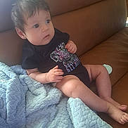 Trinity joined the competition — help win amazing prizes! baby, child, infant, couch, blanket, clothing, onesie, face, hair, skin, foot, hand, furniture, indoor, portrait, seated, curious, soft_texture, leather, relaxed