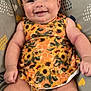baby, infant, smiling, sunflower, dress, patterned_clothing, cushion, heart_pattern, comfortable, happy, cheerful, skin, chubby, sitting, indoors, closeup, portrait, cute, child, person