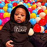 baby, ball_pit, black_clothing, bright_colors, casual_wear, child, colorful, cute, expression, fun, gap, hoodie, indoor, infant, looking, plastic_balls, play_area, portrait, seated, young_child