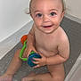 baby, bathtub, bath, child, smile, toy, water, skin, play, happy, sitting, curly_hair, young_child, indoor, bath_mat, person, cute, toddler, fun, bath_time