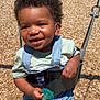 toddler, child, swing, playground, pacifier, smiling, sunlight, outdoor, curly_hair, denim_overalls, green_pacifier, wood_chips, happy, baby, shorts, clothing, play, fun, person, summer