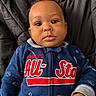 Isaiah is registered to the contest to win money with this photo: baby, black_background, blue_clothing, child, closeup, cozy, cushion, cute, expression, eyes, face, hand, indoors, infant, person, portrait, skin, sleepsuit, text_on_clothing, young
