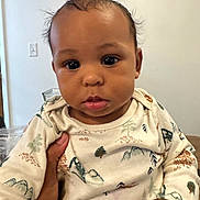 Isaiah is registered to the contest to win money with this photo: baby, infant, child, face, hand, onesie, clothing, pattern, mountains, trees, indoor, person, portrait, cute, curly_hair, expression, skin, young, holding, background