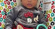 Isaiah joined the competition — help win amazing prizes! baby, bouncer, child, colorful, comfort, curly_hair, cute, expression, face, hand, indoor, infant, mickey_mouse, patterned_background, red_pants, seated, sweatshirt, teething_toy, toy, young