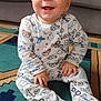 Hugo participe au concours pour gagner de l'argent avec cette photo : baby, child, smiling, onesie, patterned_clothing, sitting, carpet, rug, indoor, couch, furniture, happy, face, hands, footed_pajamas, floor, toy_car, home, cute, toddler