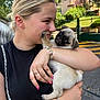 woman, puppy, dog, pug, pet, outdoor, smile, affection, bracelet, ring, black_shirt, chain_strap, cute, face, holding, playing, greenery, building, daylight, happy