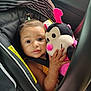toddler, child, car_seat, plush_toy, ladybug, toy, seatbelt, hair_tie, indoor, person, cute, smiling, baby, childrens_toy, black_fabric, striped_pattern, pink, yellow_warning_label, closeup, car_interior