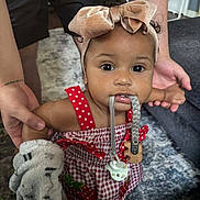 Mya is registered to the contest to win money with this photo: toddler, child, baby, headband, bow, dress, red, checkered, strawberry, pacifier, soft_toy, indoor, carpet, adult_hands, curly_hair, cute, holding, playful, support, person