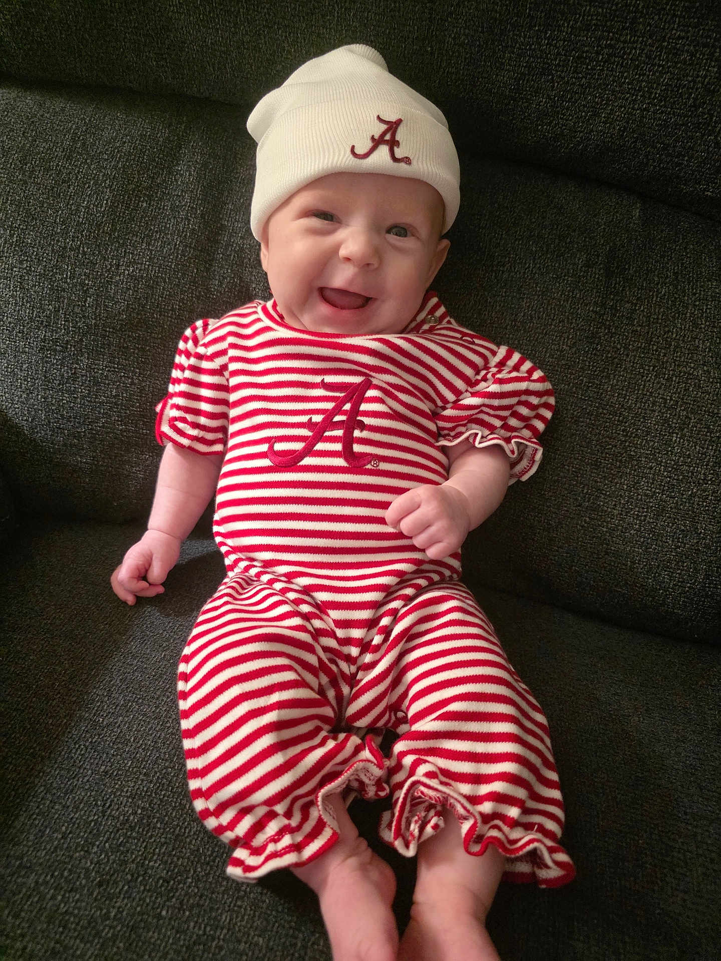 Scarlett joined the competition — help win amazing prizes! baby, smiling, infant, striped_clothing, hat, red_and_white, sitting, couch, happy, cute, child, face, apparel, cozy, indoor, person, portrait, young, fun, relaxed