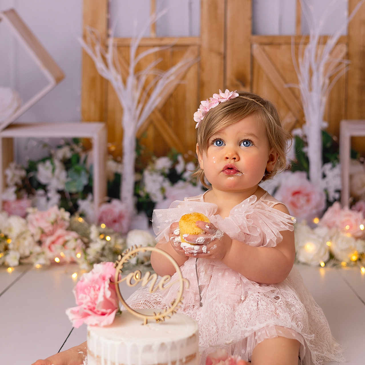 Emma a rejoint le concours — aidez-le/la à gagner de superbes lots ! baby, birthday, blue_eyes, cake, celebration, child, cupcake, cute, decorations, first_birthday, flower_headband, flowers, indoor, pink_dress, portrait, sitting, smudged_frosting, toddler, white_floor, wooden_backdrop