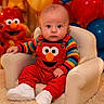 Apollo is registered to the contest to win money with this photo: baby, child, infant, elmo, red_overalls, striped_shirt, white_shoes, armchair, balloons, plush_toy, carpet, indoor, celebration, portrait, cute, colorful, smile, face, person, seated