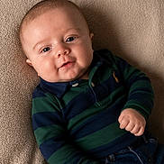 Apollo is registered to the contest to win money with this photo: baby, blanket, blue, child, cute, face, green, hand, happy, indoors, infant, jeans, person, polo_shirt, portrait, relaxed, smile, striped_clothing, texture, young_child
