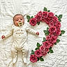 baby, infant, pacifier, onesie, text_on_clothing, flower_arrangement, roses, green_leaves, blanket, white_background, cute, lying_down, portrait, child, soft_texture, floral_design, decorative, pink_flowers, natural_elements, adorable