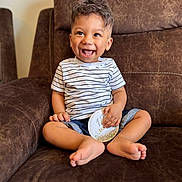 Zidan is registered to the contest to win money with this photo: toddler, child, smiling, sitting, striped_shirt, shorts, barefoot, couch, indoor, happy, curly_hair, milestone_card, brown_furniture, portrait, cute, young_child, casual, comfortable, baby, joyful